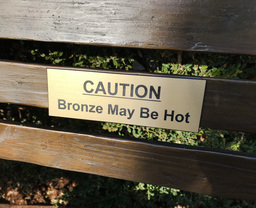 A caution sign on a wooden bench warning that the bronze may be hot.